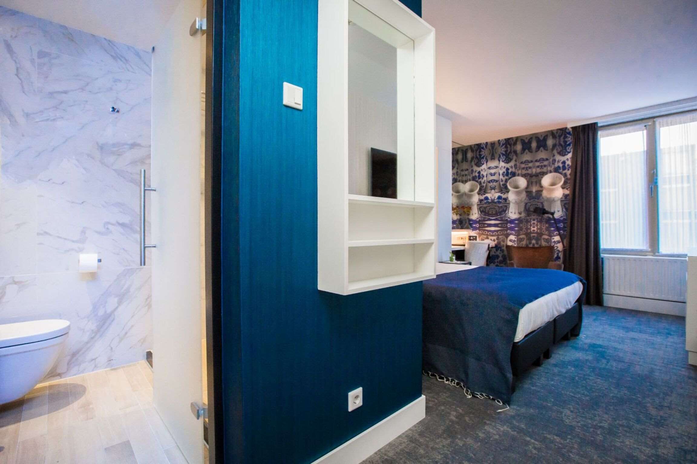 Une chambre d’hôtel avec une salle de bain, un lit, une table de chevet et une fenêtre avec des rideaux.