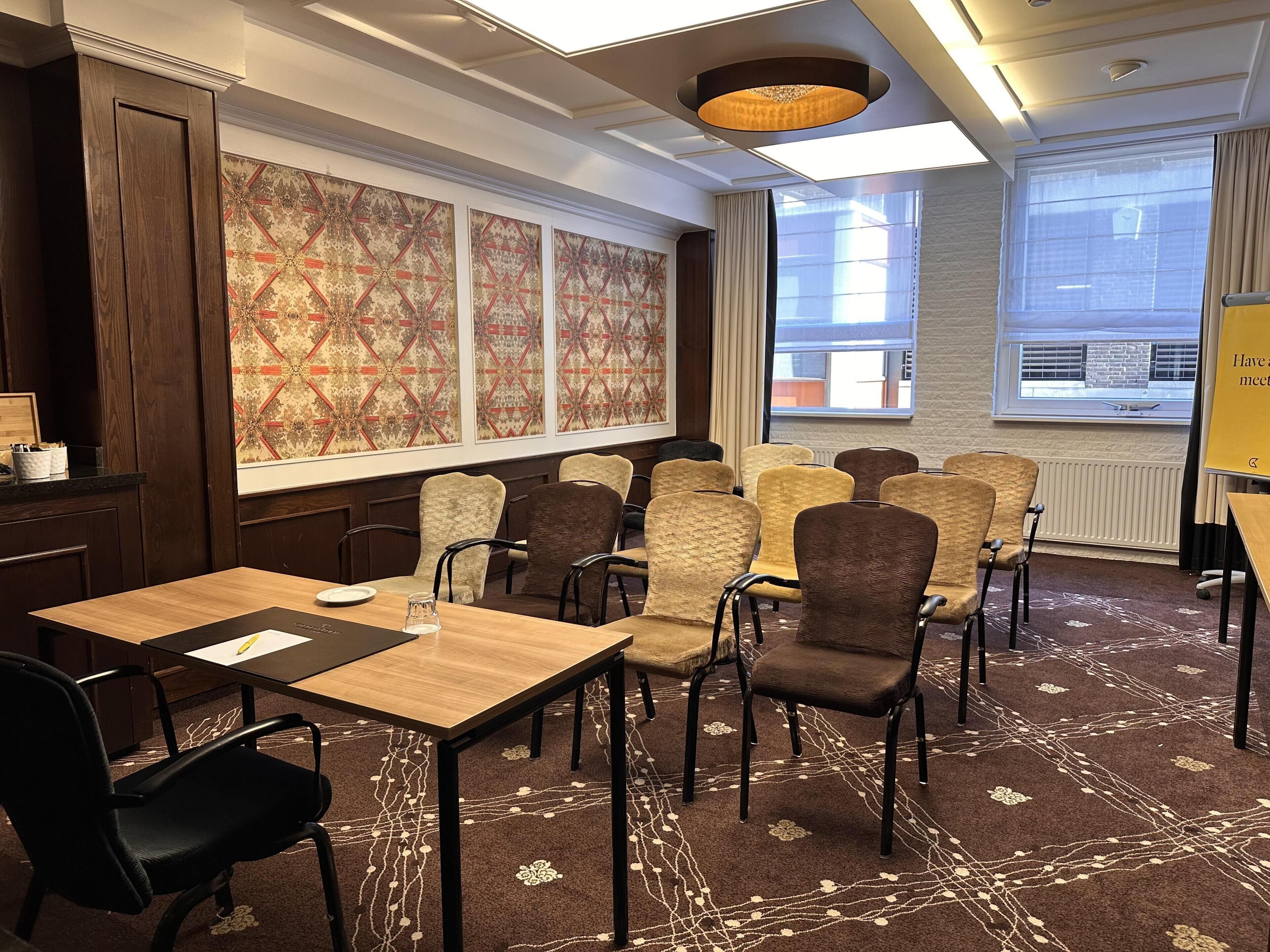 Une salle de conférence avec une longue table, de nombreuses chaises, un mur orné de motifs et de grandes fenêtres.