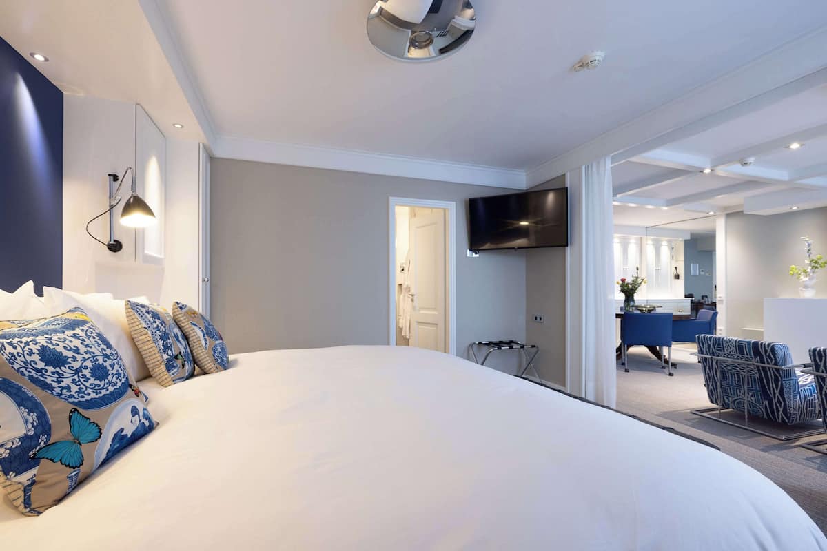 A modern hotel room with a large bed, a flat-screen TV mounted on the wall, and a desk area with a chair.