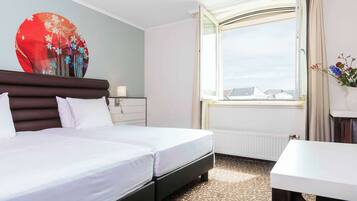 A hotel room with a bed, a bedside table, a window with curtains, and a wall decoration.