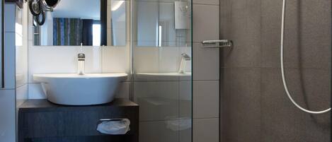 Un baño moderno con ducha envuelta en vidrio, un lavabo blanco y un espejo sobre él.