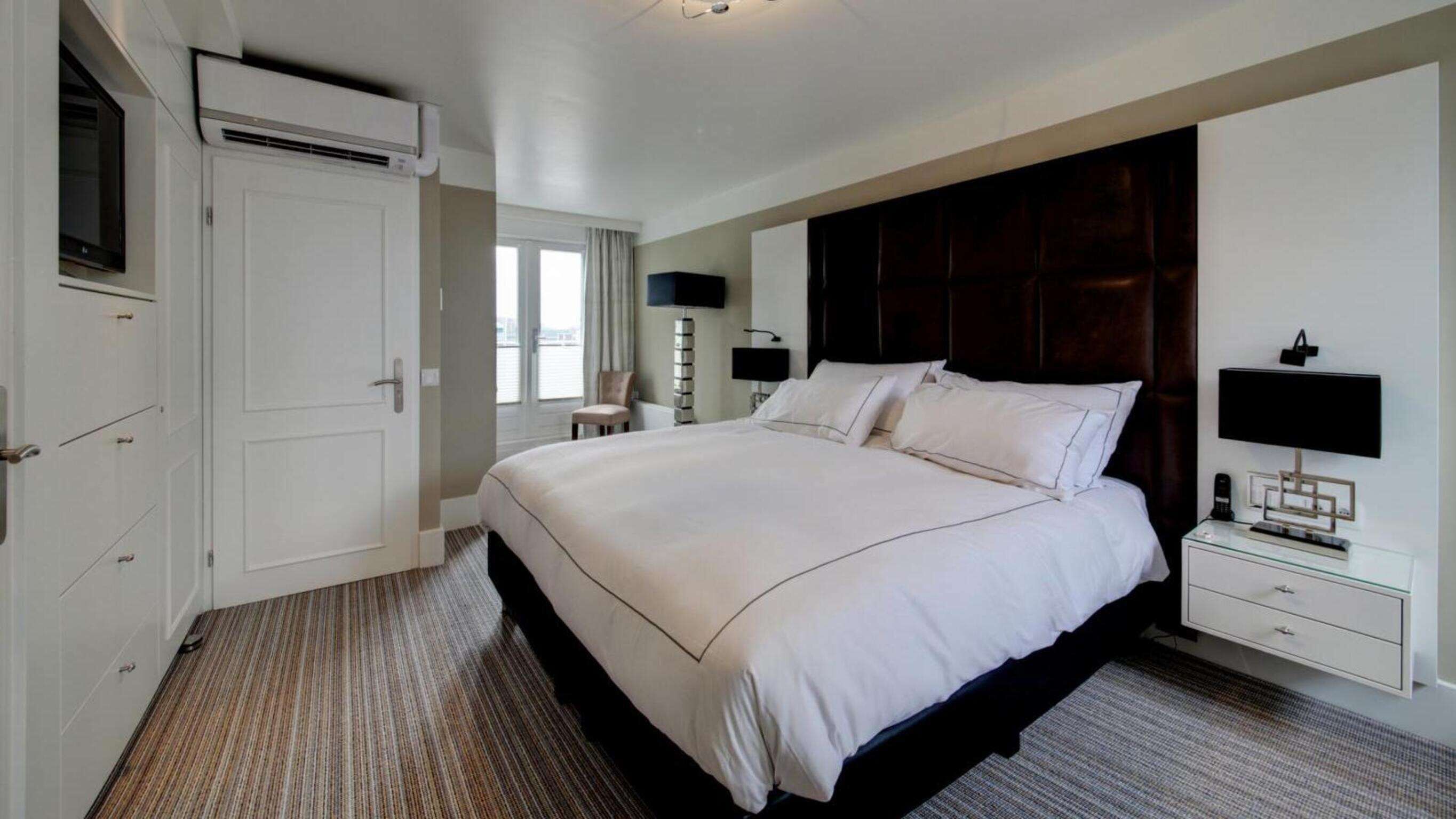 A hotel room with a large bed, a wardrobe, a desk with a lamp, and a television.