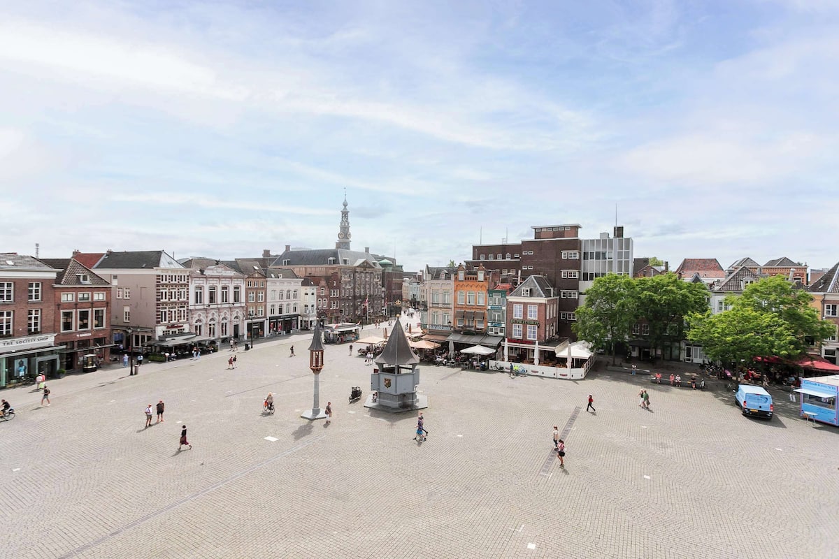 A spacious square with historic buildings, a prominent tower, and a central monument.