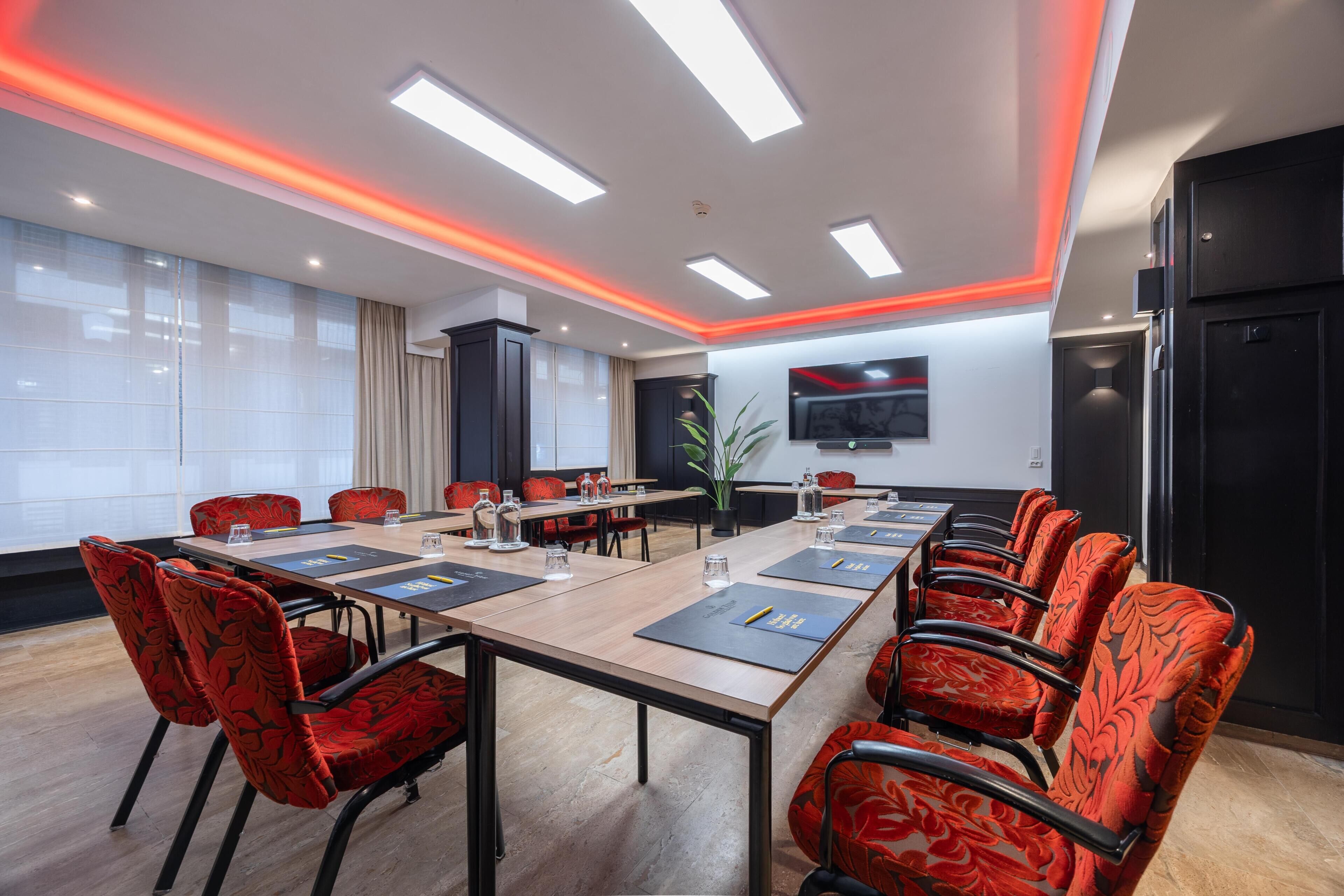 Una sala conferenze con un lungo tavolo, sedie imbottite rosse, una TV a schermo piatto e un design moderno del soffitto.
