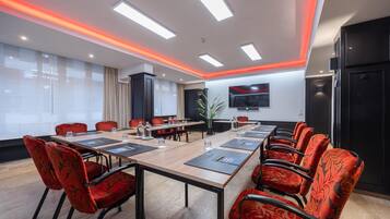 Una sala conferenze con un lungo tavolo, sedie imbottite rosse, una TV a schermo piatto e un design moderno del soffitto.