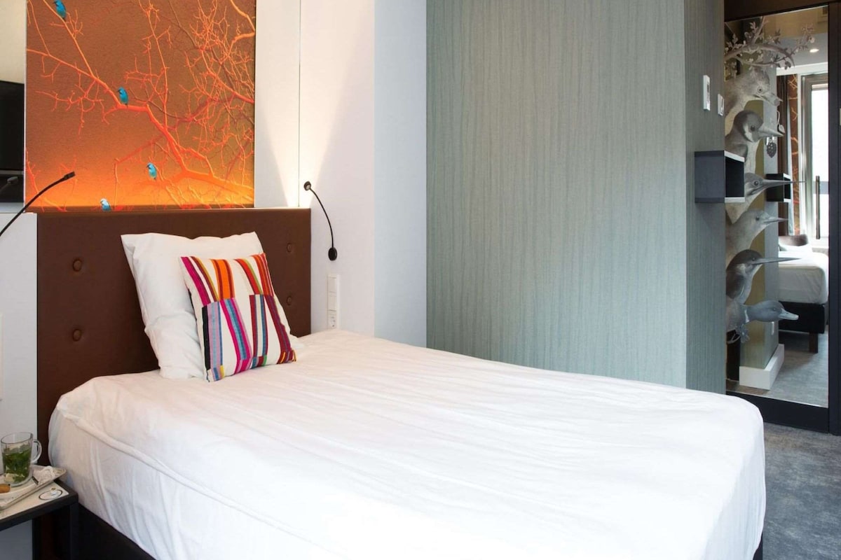 A hotel room with a large bed, a wall-mounted TV, and a decorative wall piece.