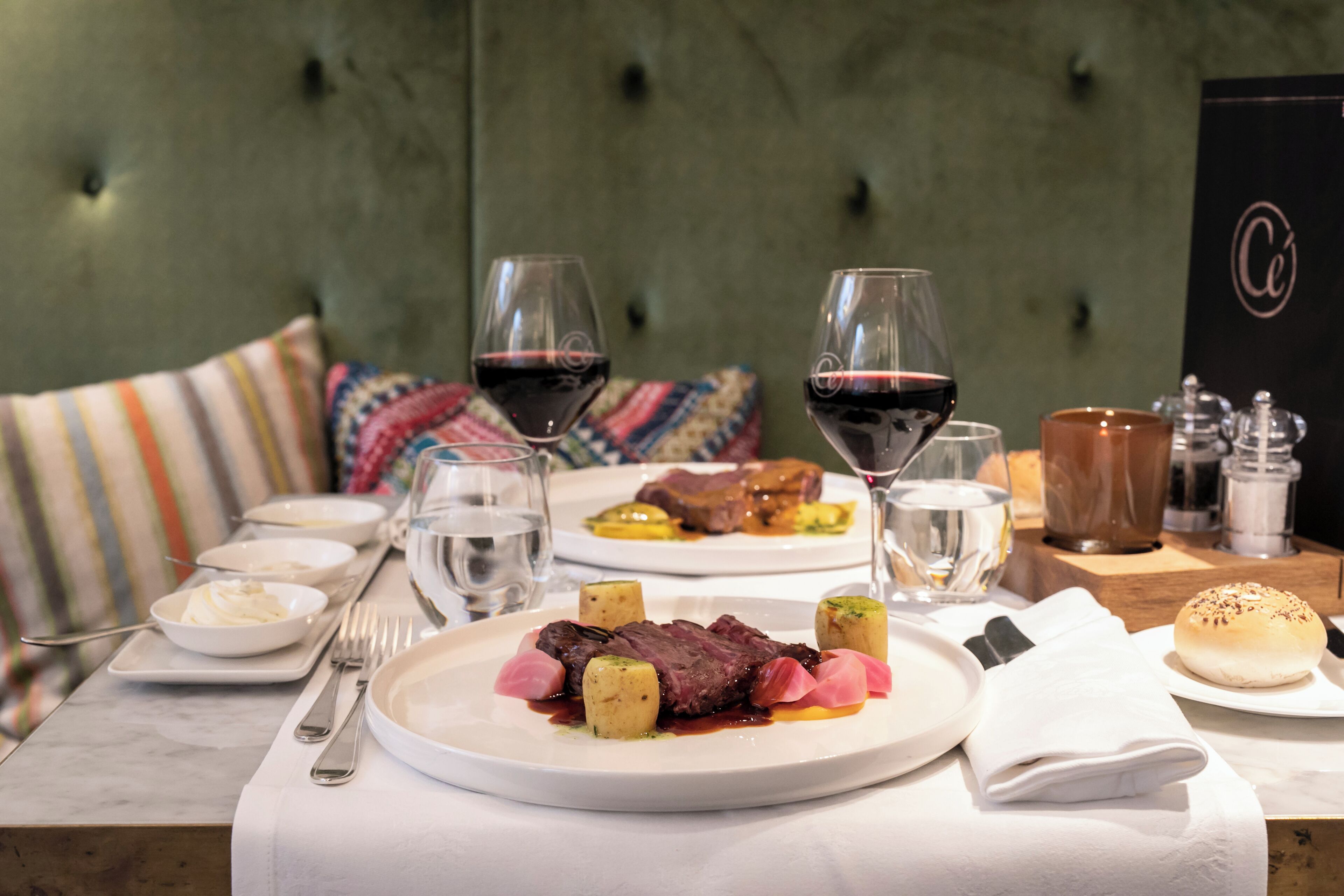 A dining table set with plates of food, wine glasses, and cutlery.