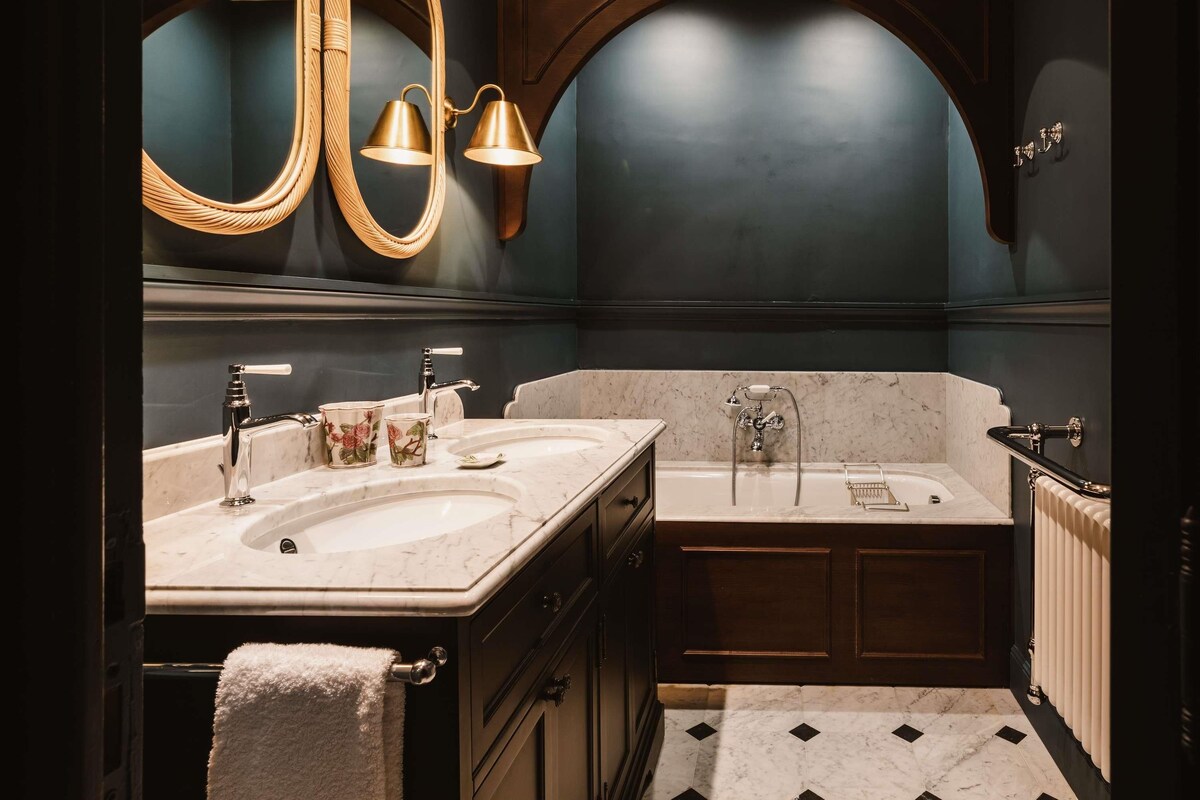 Un baño con dos lavamanos, una bañera, un espejo grande y apliques de pared.