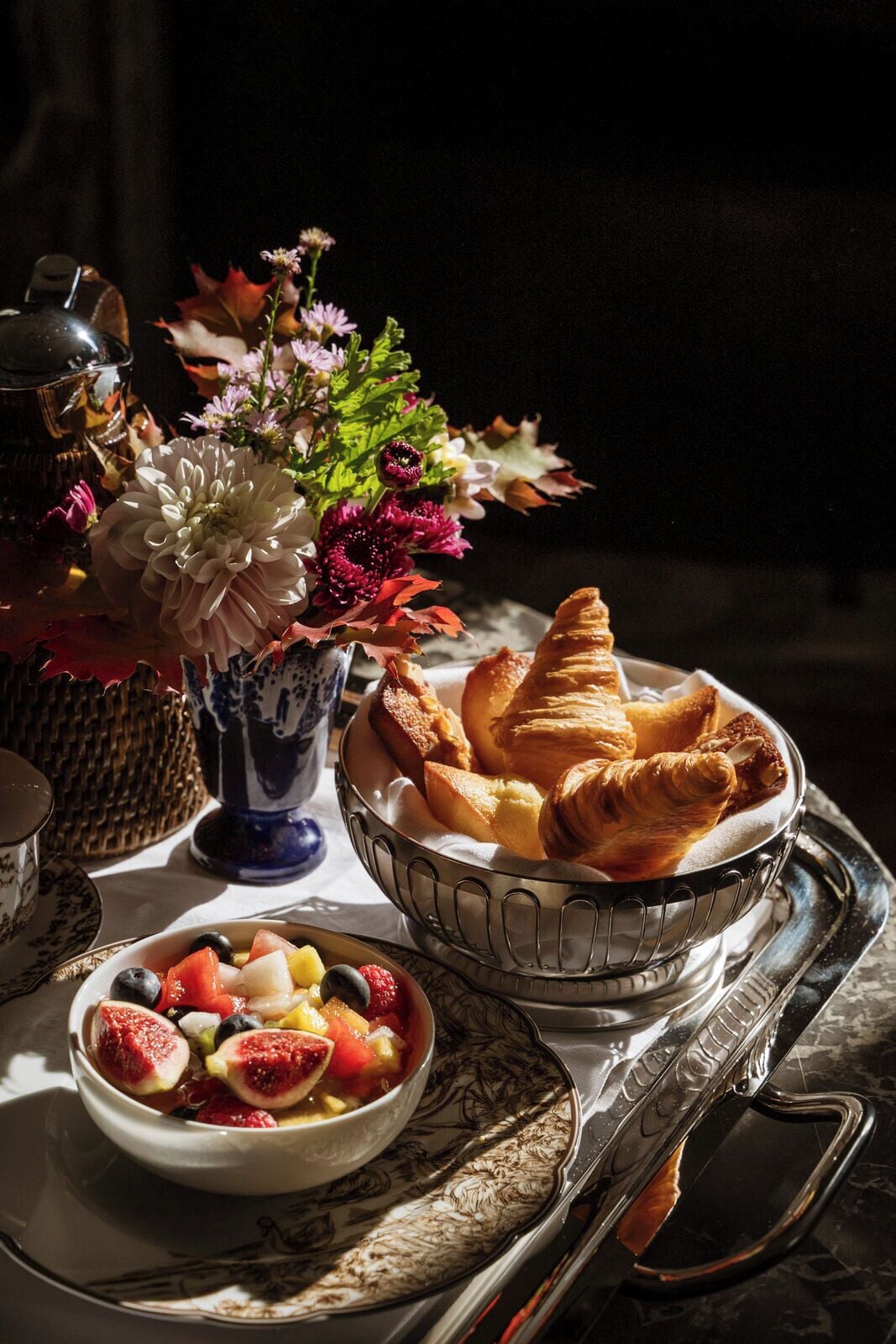 A breakfast setting with pastries, a fruit bowl, and a vase of flowers.