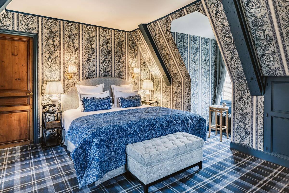 A bedroom with a bed, two bedside tables, a bench, and patterned wallpaper.