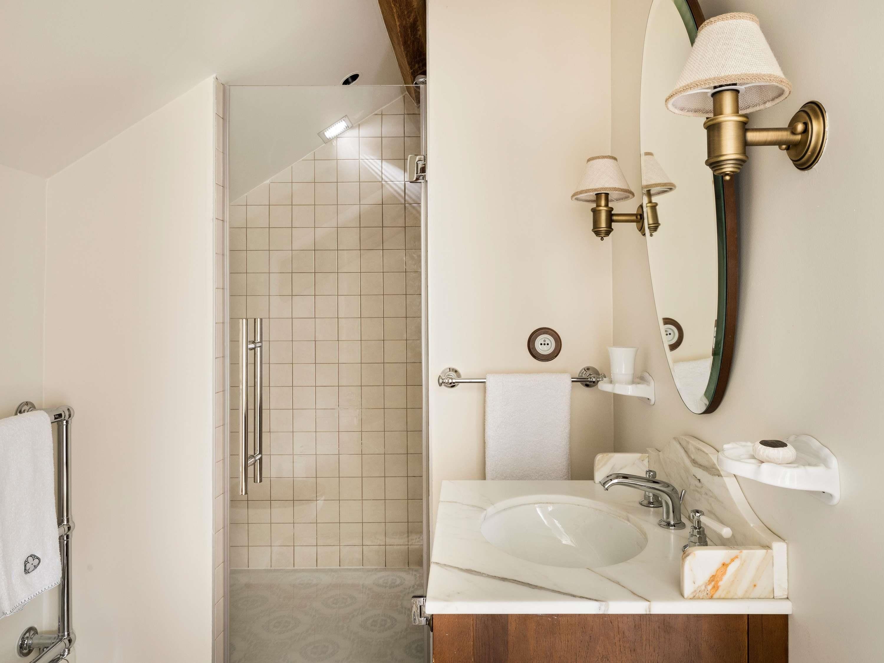 A bathroom with a glass-enclosed shower, a marble sink, a towel rack, a mirror, and a wall-mounted light fixture.