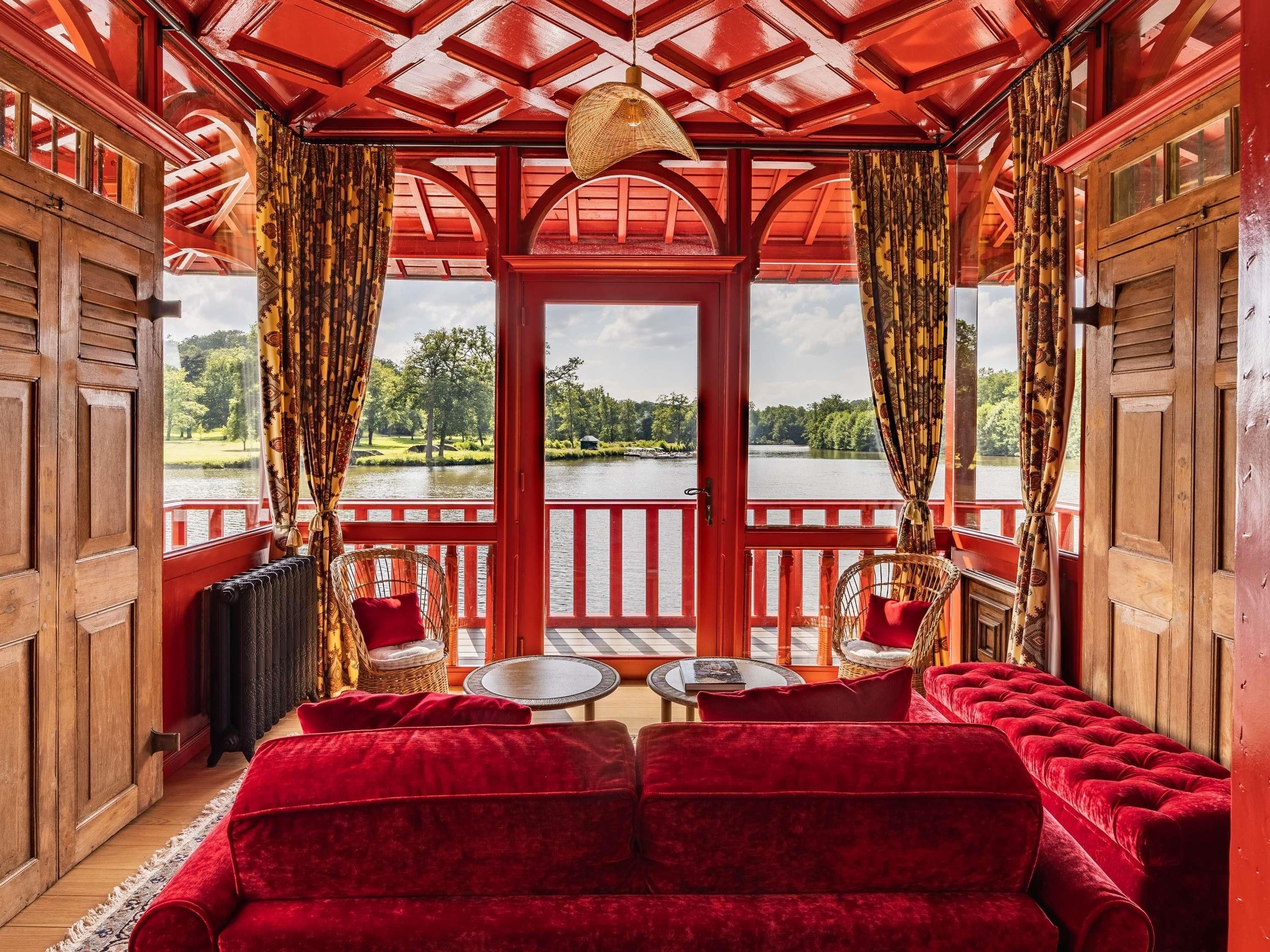 Ein Zimmer mit rotem Holzinterieur, einem großen Fenster mit Seeblick und einem roten Sofa.