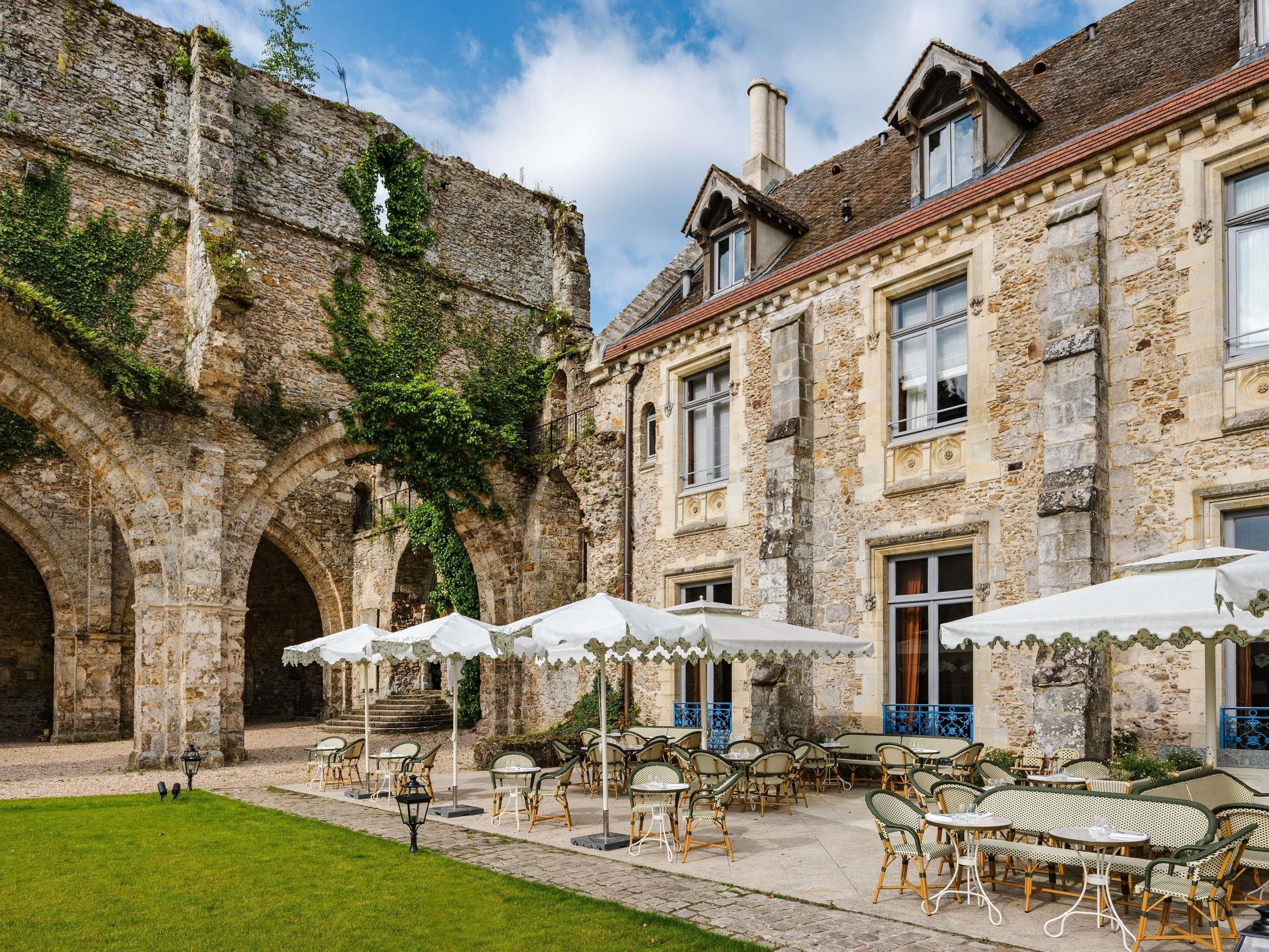 A courtyard with stone arches, outdoor seating with umbrellas, and a building with multiple windows.