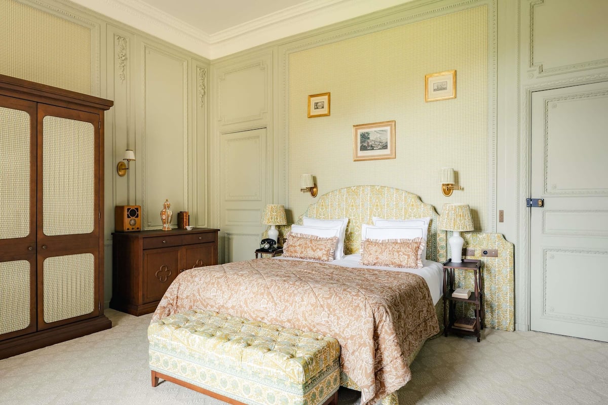 A bedroom with a large bed, a wooden wardrobe, a nightstand, and a wall-mounted lamp.