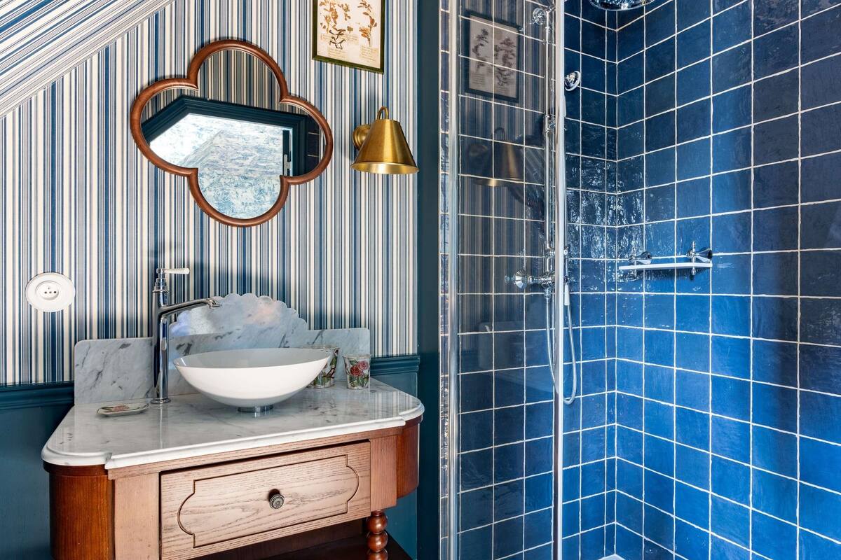 A bathroom with a sink, vanity, mirror, shower, and blue tiled walls.