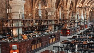 Un comedor espacioso y bien iluminado con techos altos y arcos de piedra, que cuenta con varias mesas y una zona de bar central con diferentes botellas y copas.