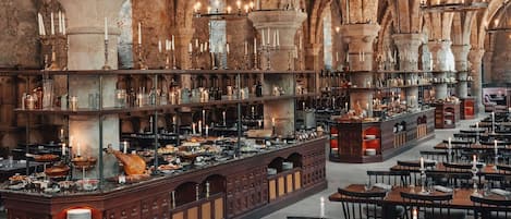 Un comedor espacioso y bien iluminado con techos altos y arcos de piedra, que cuenta con varias mesas y una zona de bar central con diferentes botellas y copas.