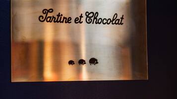 Un senyal metàl·lic amb el text "KIDS CLUB" i "Tartine et Chocolat", acompanyat de dos icones de eriçons.