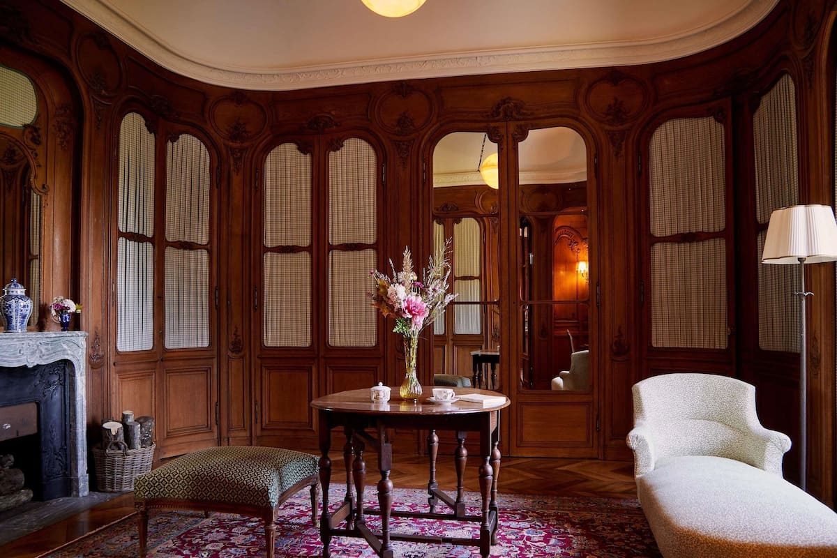 A room with a round table, a chair, a vase with flowers, and a fireplace.