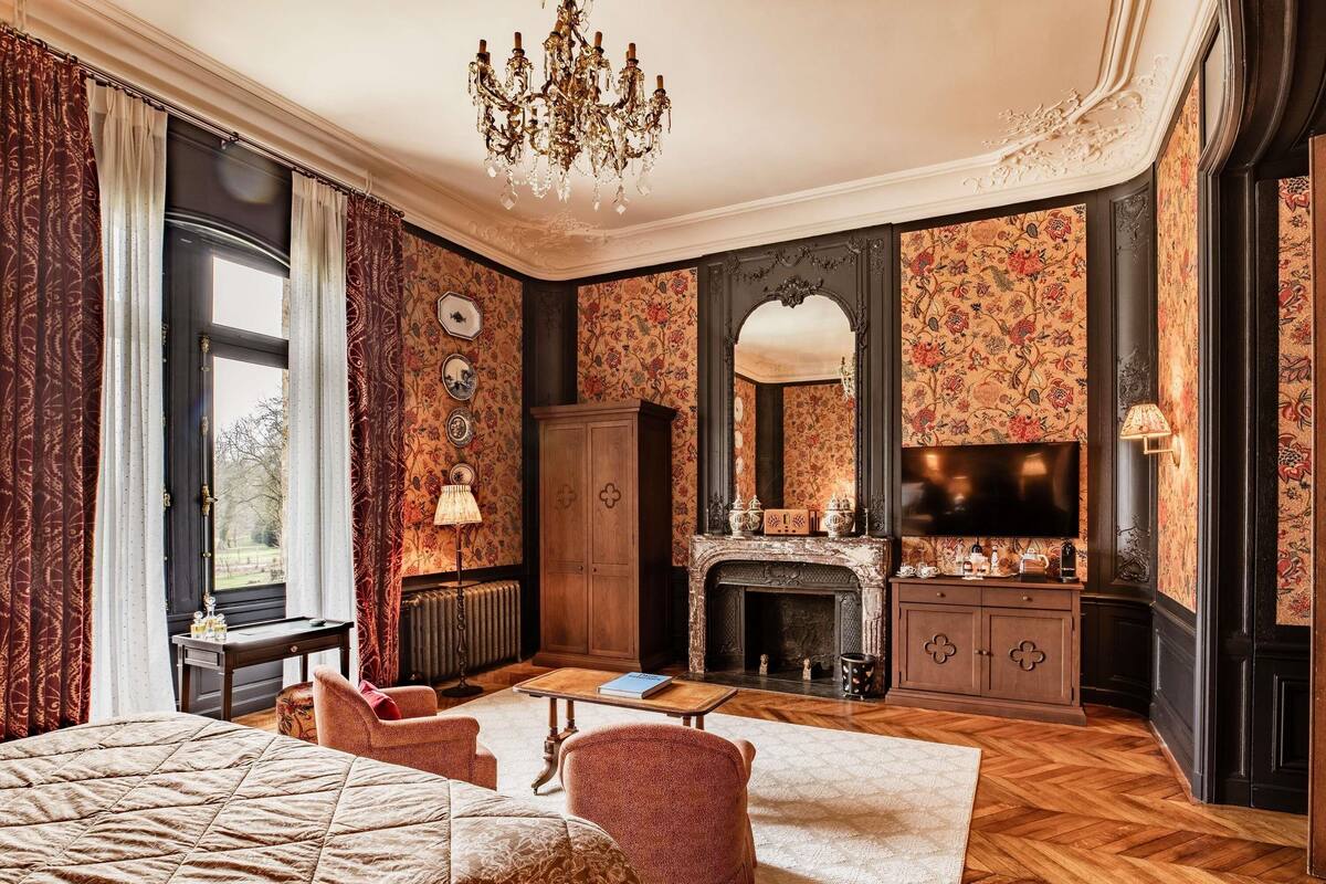A bedroom with a large bed, a fireplace, a television, and a chandelier.