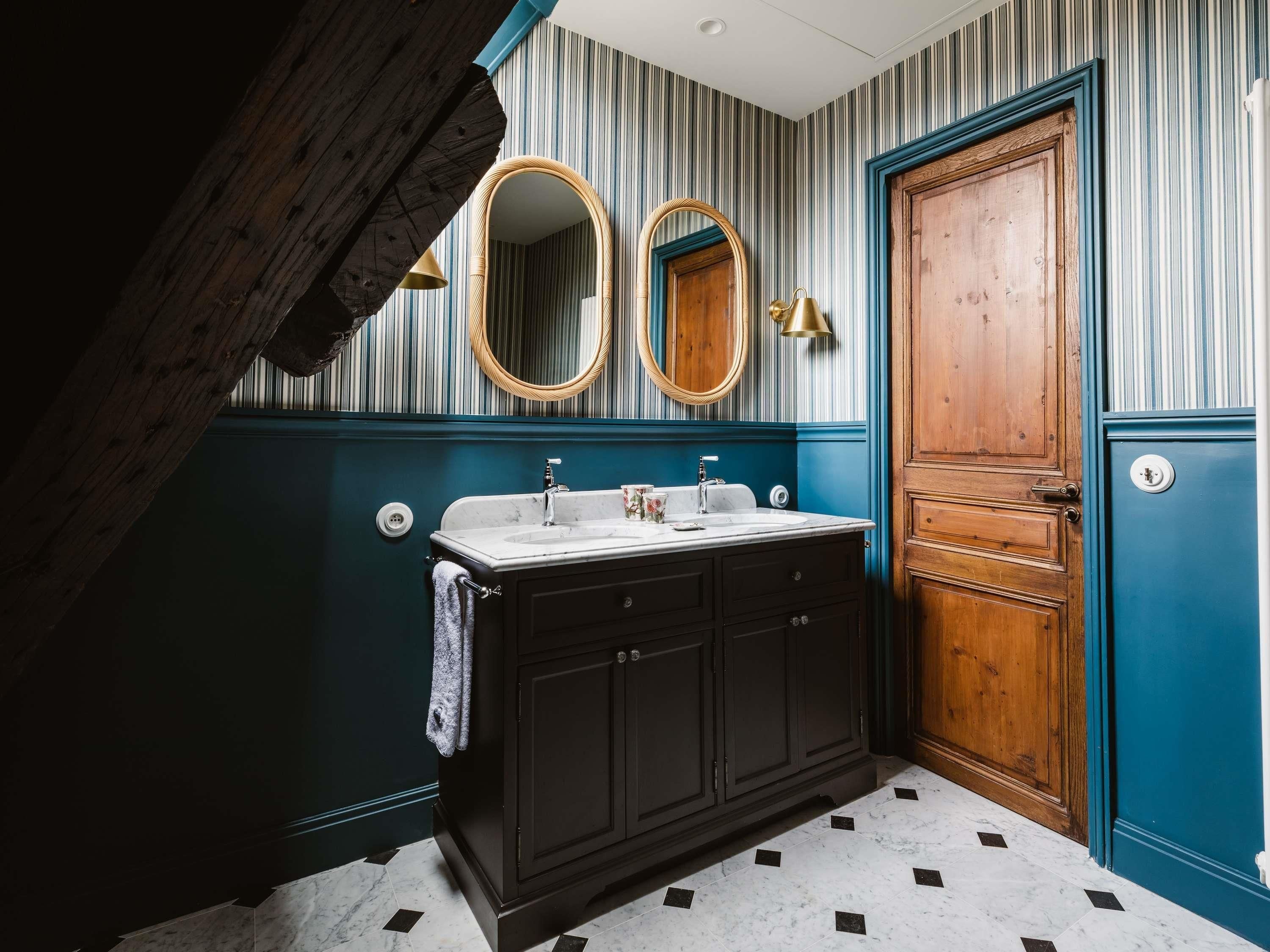A bathroom with a dark wooden vanity, two sinks, a mirror, and a door with a keyhole.