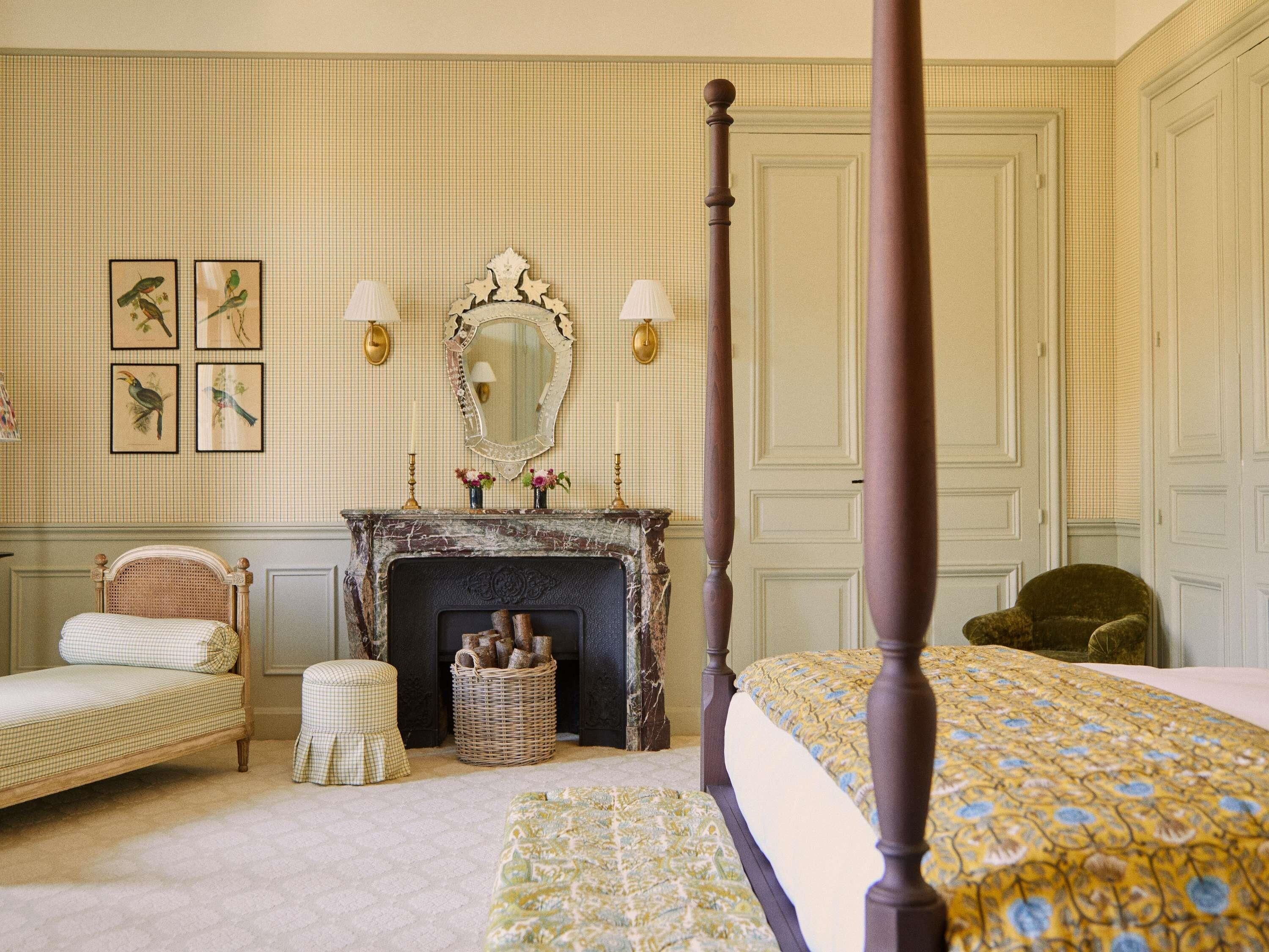 A bedroom with a four-poster bed, a fireplace, a mirror, and wall-mounted lamps.