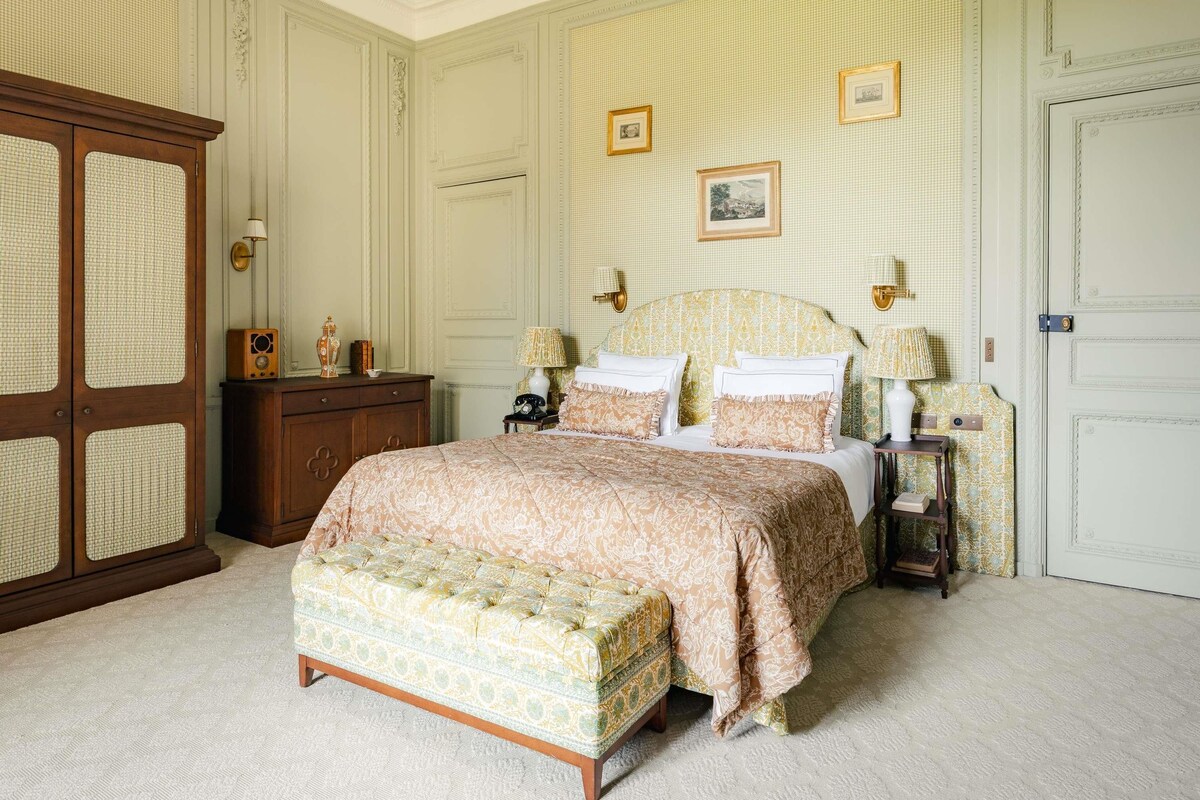 A bedroom with a large bed, a wooden wardrobe, a nightstand, and a wall-mounted lamp.