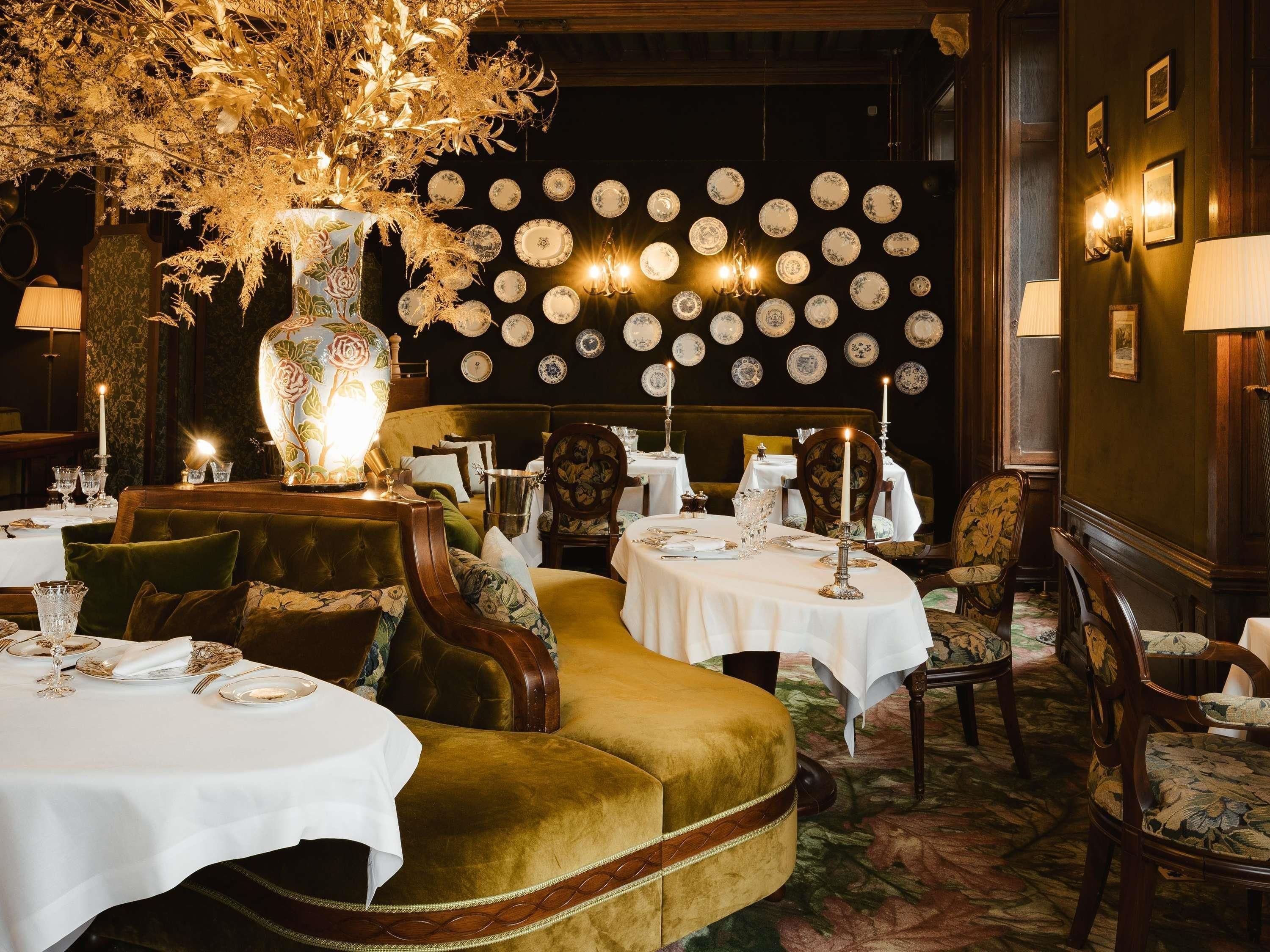 A dining area with round tables, velvet sofas, and a wall decorated with plates.