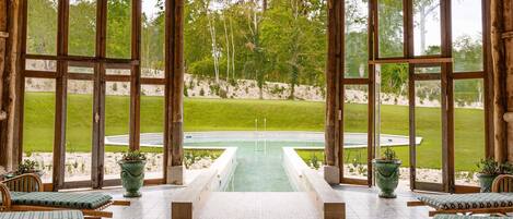 A rustic wooden gazebo with a pool view, wooden benches, and potted plants.
