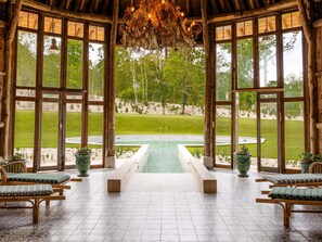 A rustic wooden gazebo with a pool view, wooden benches, and potted plants.