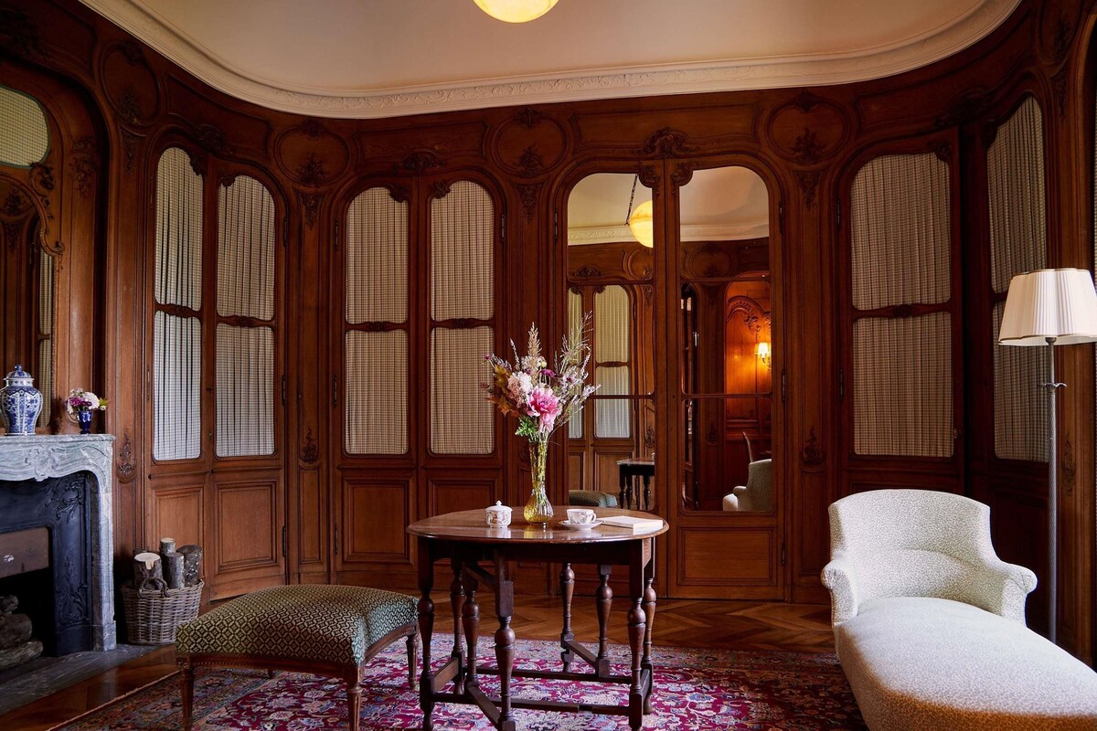 Une pièce avec une table ronde, une chaise, un vase de fleurs et une cheminée.