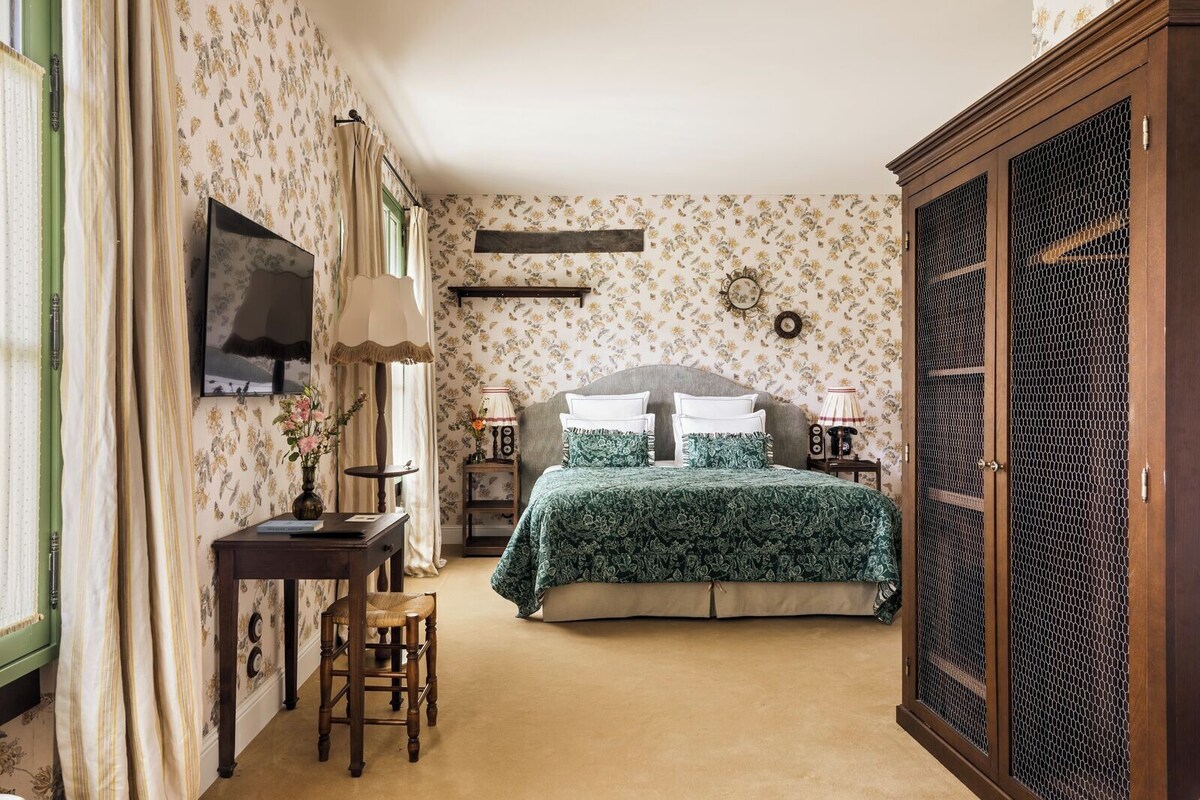 Een slaapkamer met een bed, een bureau, een stoel, een kledingkast en een televisie aan de muur.