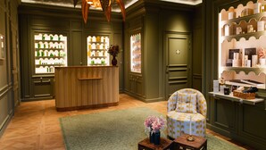 Un espace d’accueil comprenant un comptoir de réception en bois, un fauteuil à motifs floraux et une petite table sur laquelle est posé un vase rempli de fleurs.