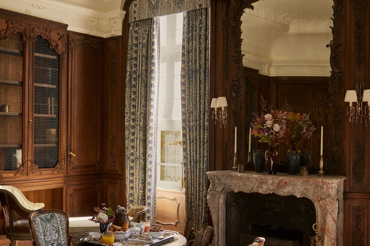 Classic room with a round table, upholstered chairs, and a large mirror above the fireplace.