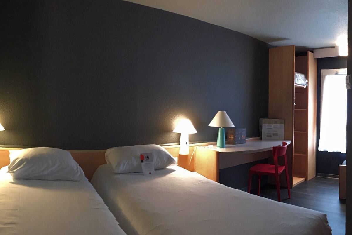 A hotel room with two beds, a desk, a chair, and a wardrobe.