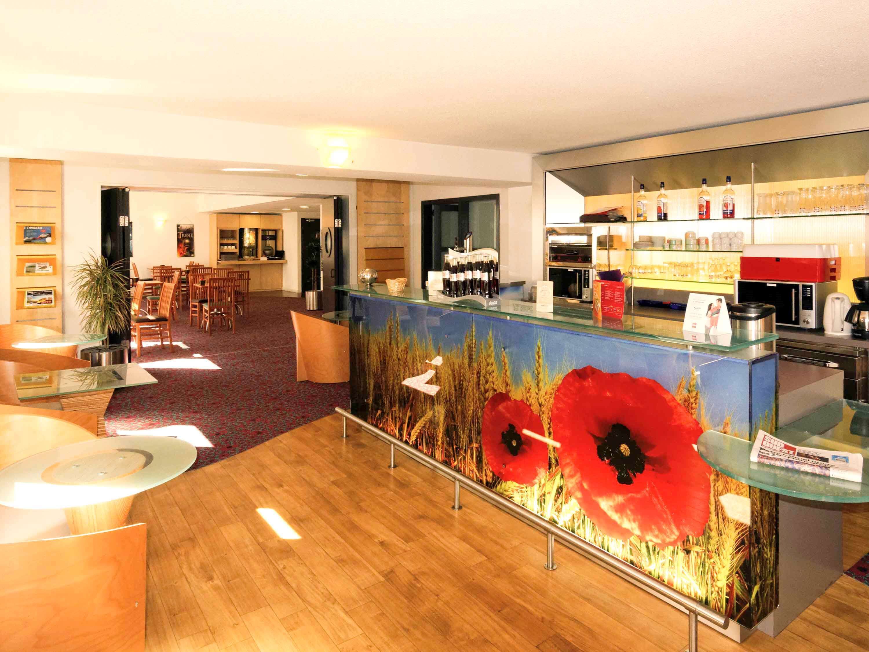 A hotel lobby with a reception desk, seating area, and a kitchen visible in the background.