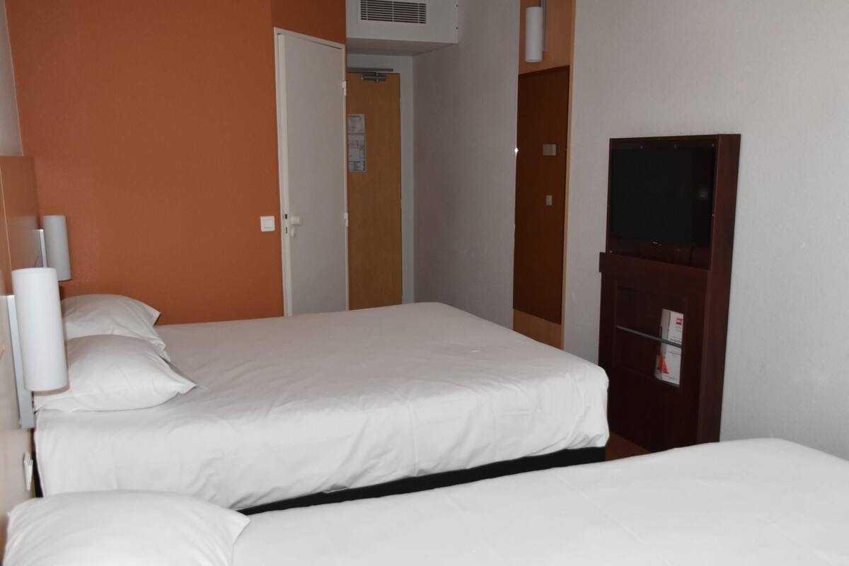 A hotel room with two beds, a wooden wardrobe, a television, and a door leading to another room.