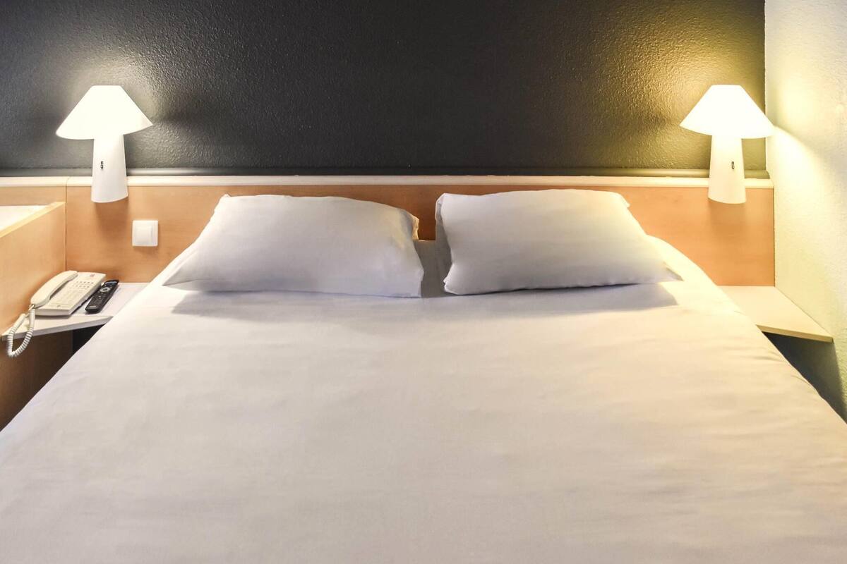 A hotel room with a bed, two bedside lamps, a phone, and a wall-mounted light fixture.