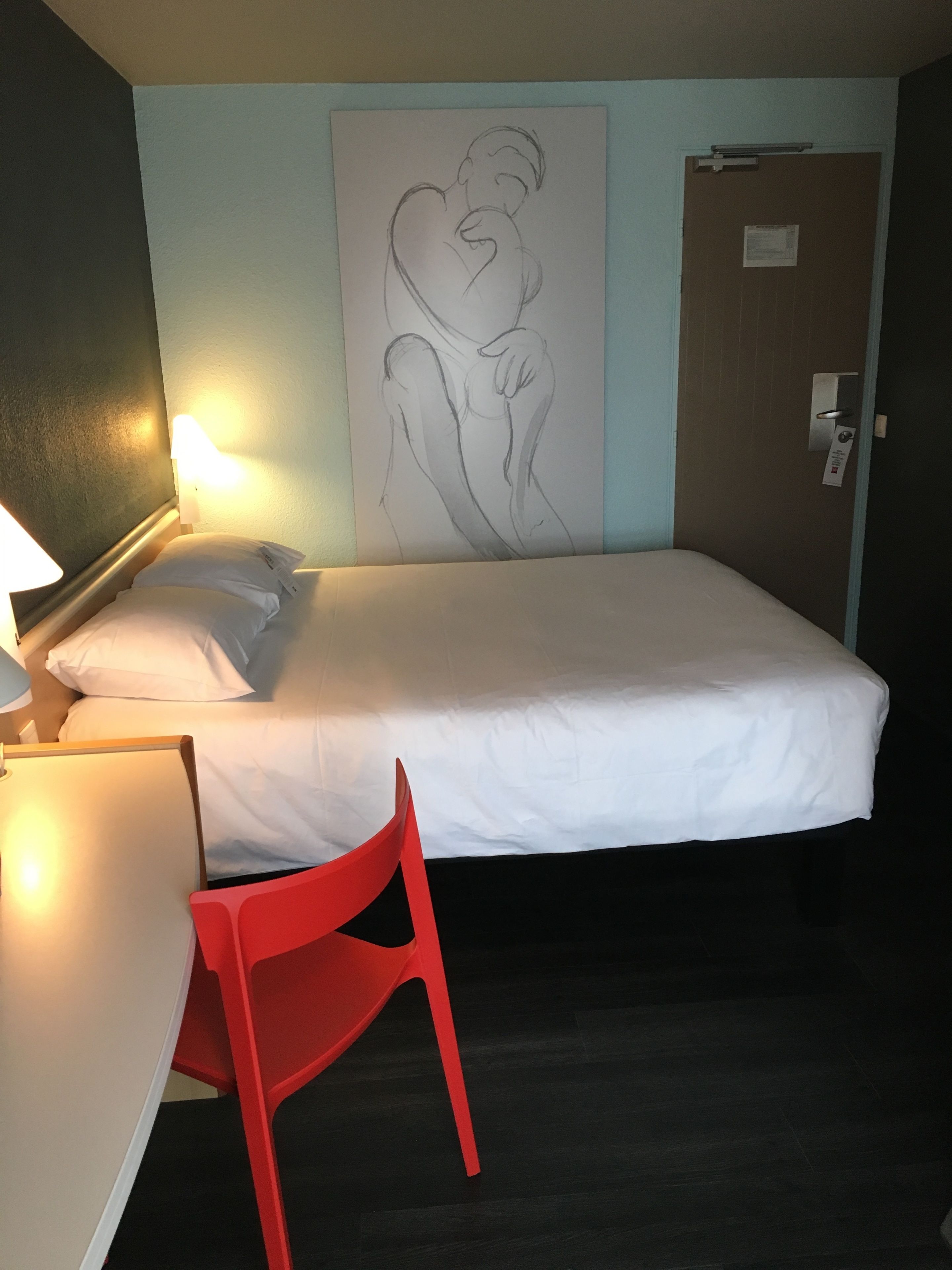 Ein Hotelzimmer mit Bett, Schreibtisch, Stuhl und einem Wandbild.