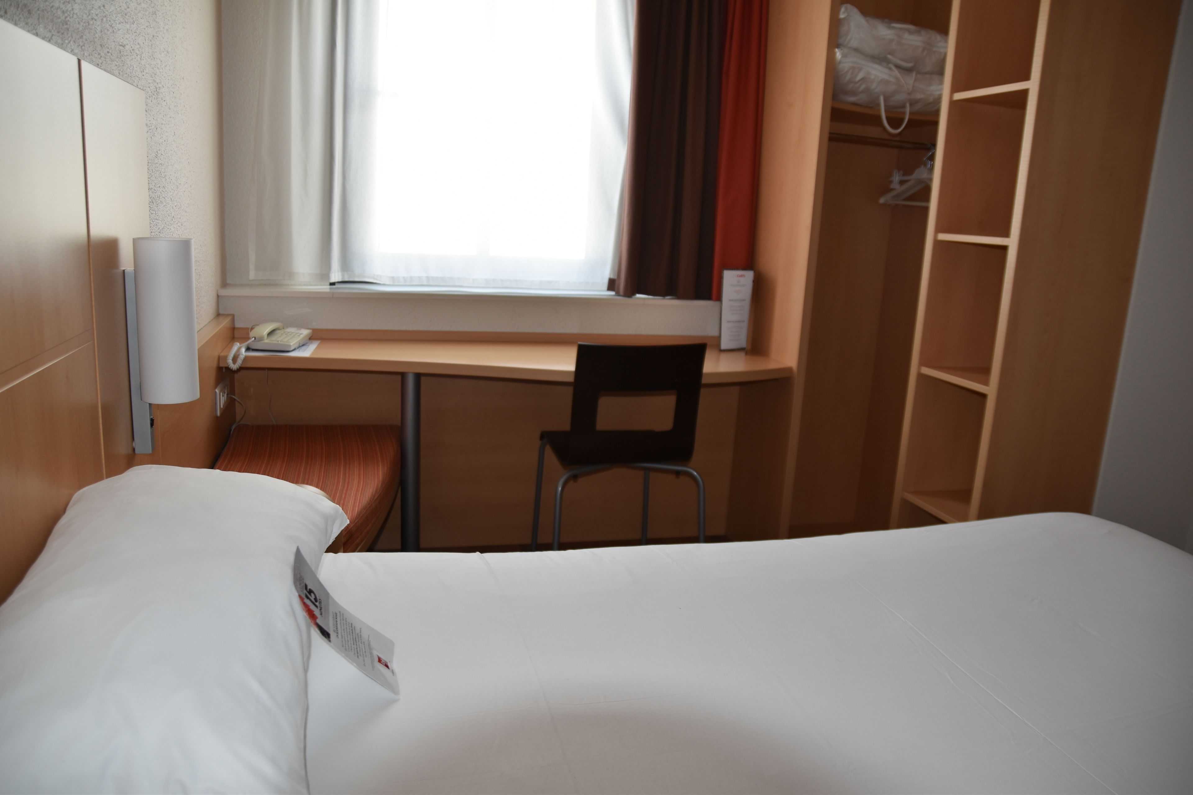 Habitación de hotel con cama, escritorio, silla, teléfono y ventana con cortinas.