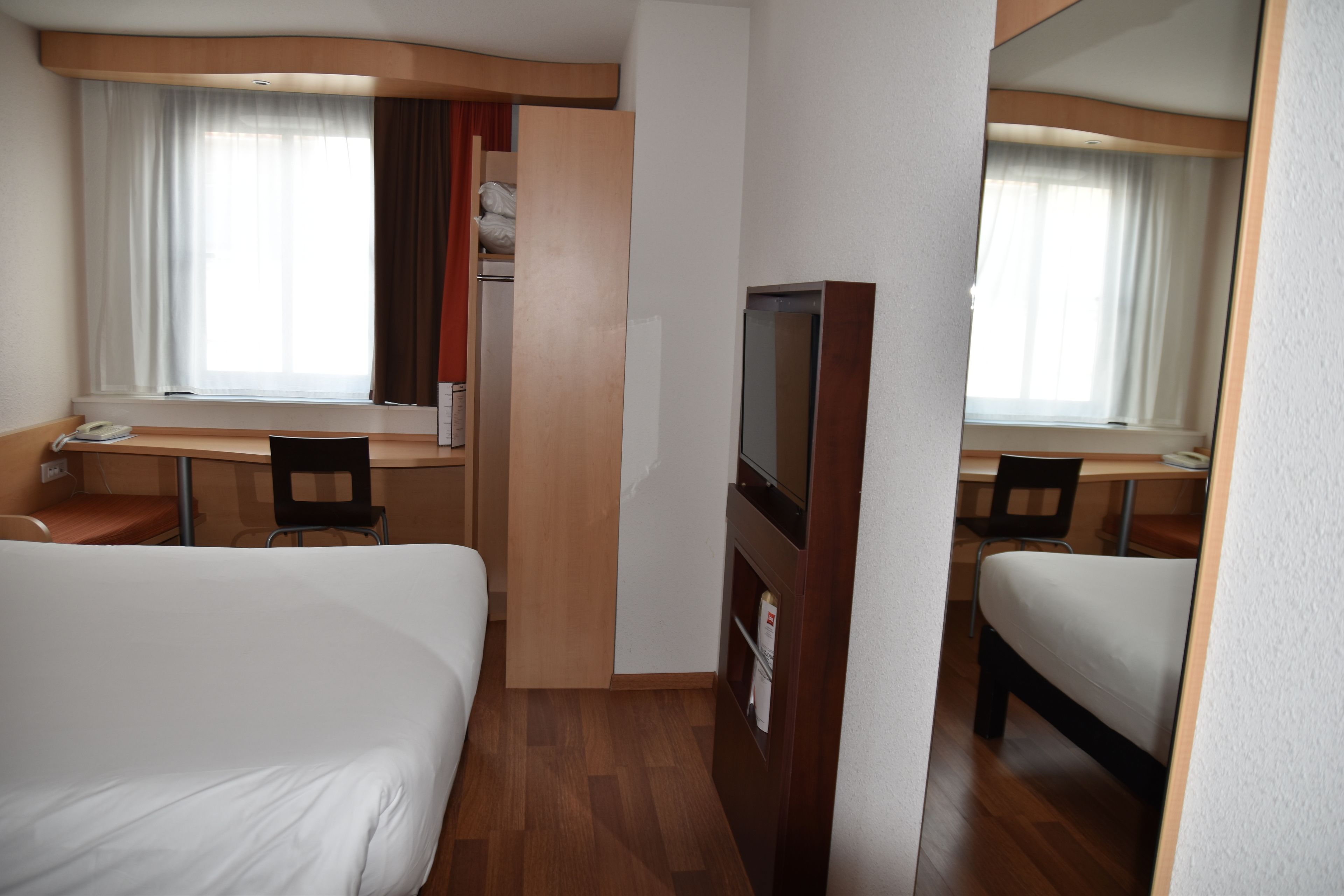 Ein Hotelzimmer mit einem Bett, einem Schreibtisch, einem Sessel, einem Fernseher und einem Kleiderschrank.