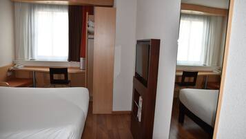 Una habitación de hotel con cama, escritorio, silla, televisor y armario.