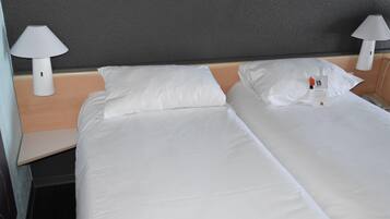 A hotel room with two beds, white linens, and two bedside lamps.
