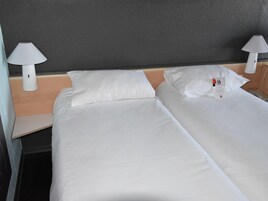 A hotel room with two beds, white linens, and two bedside lamps.
