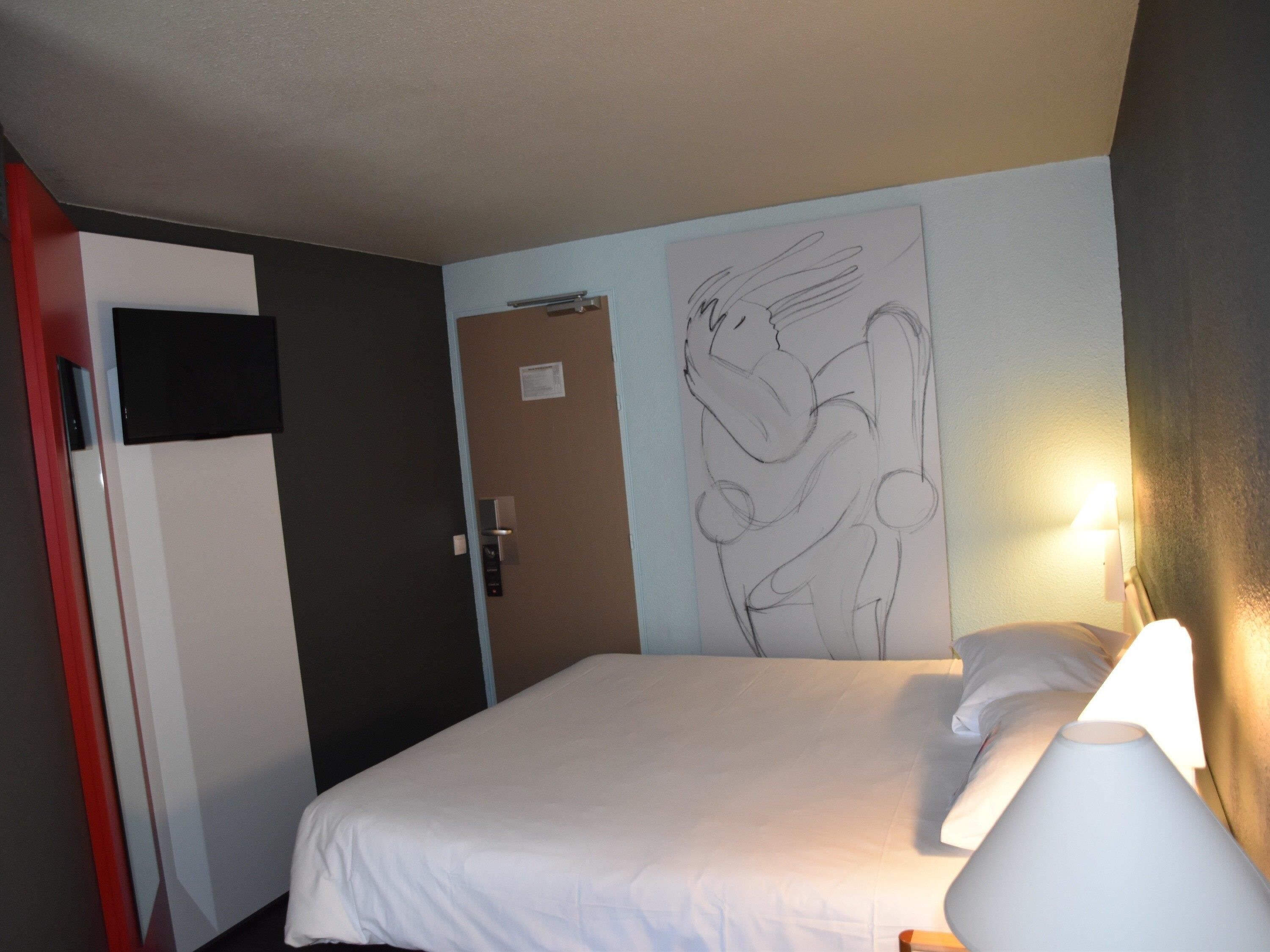 Een hotelkamer met een bed, een wandlamp, een deur en een deurbel.