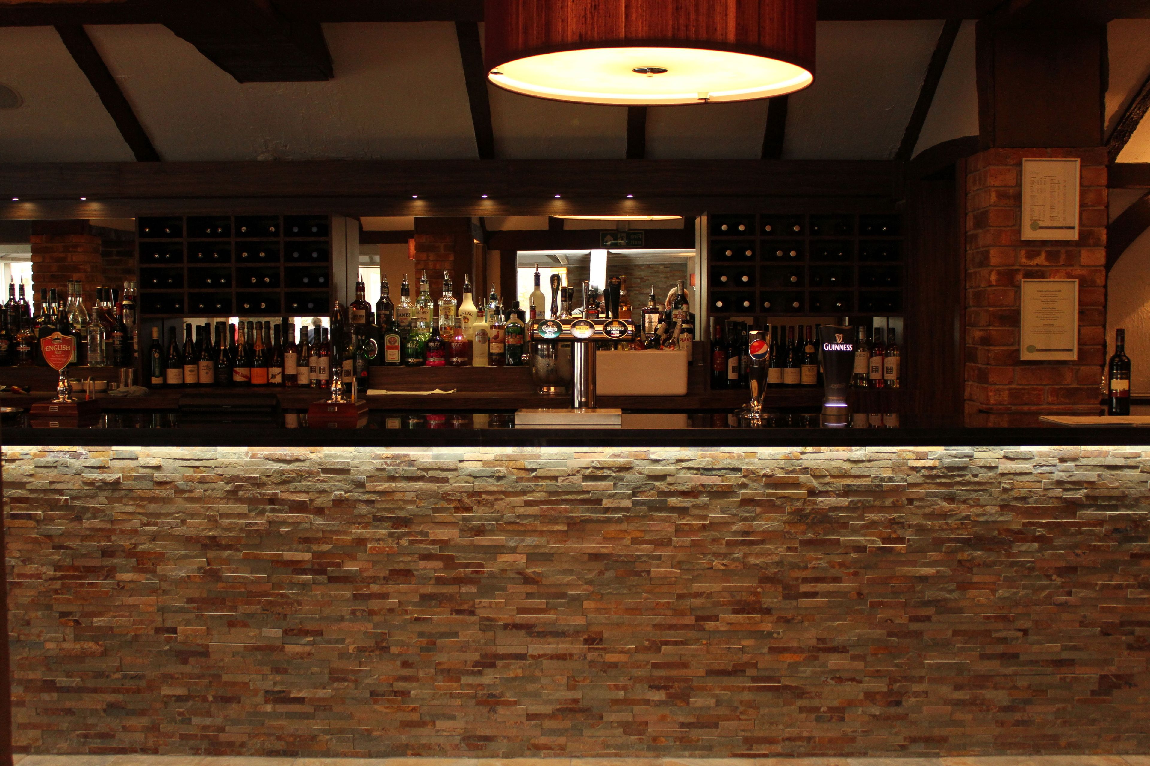 A bar area with a brick counter, various bottles, and a hanging light fixture.