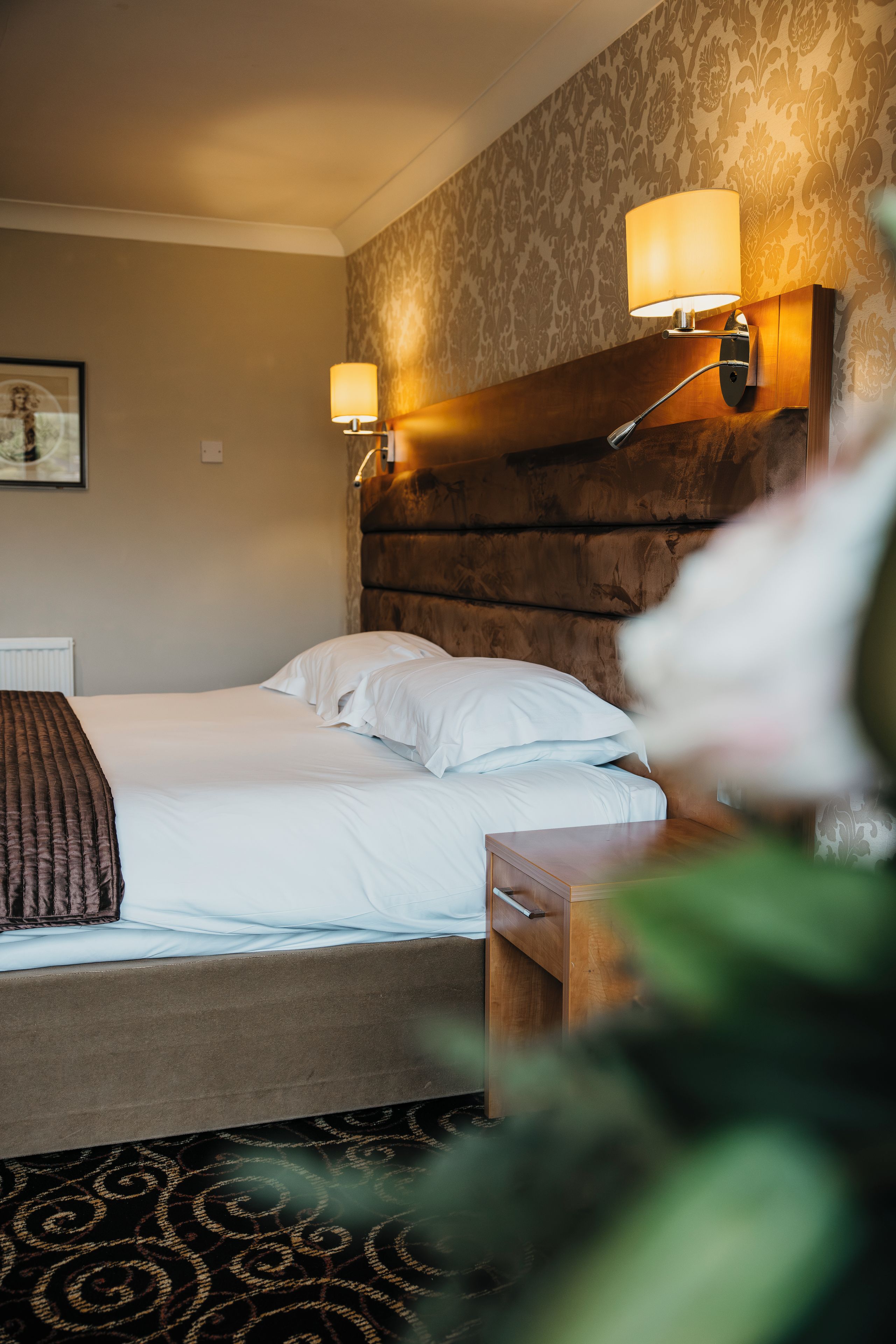 A hotel room with a bed, two bedside lamps, a headboard, and a nightstand.