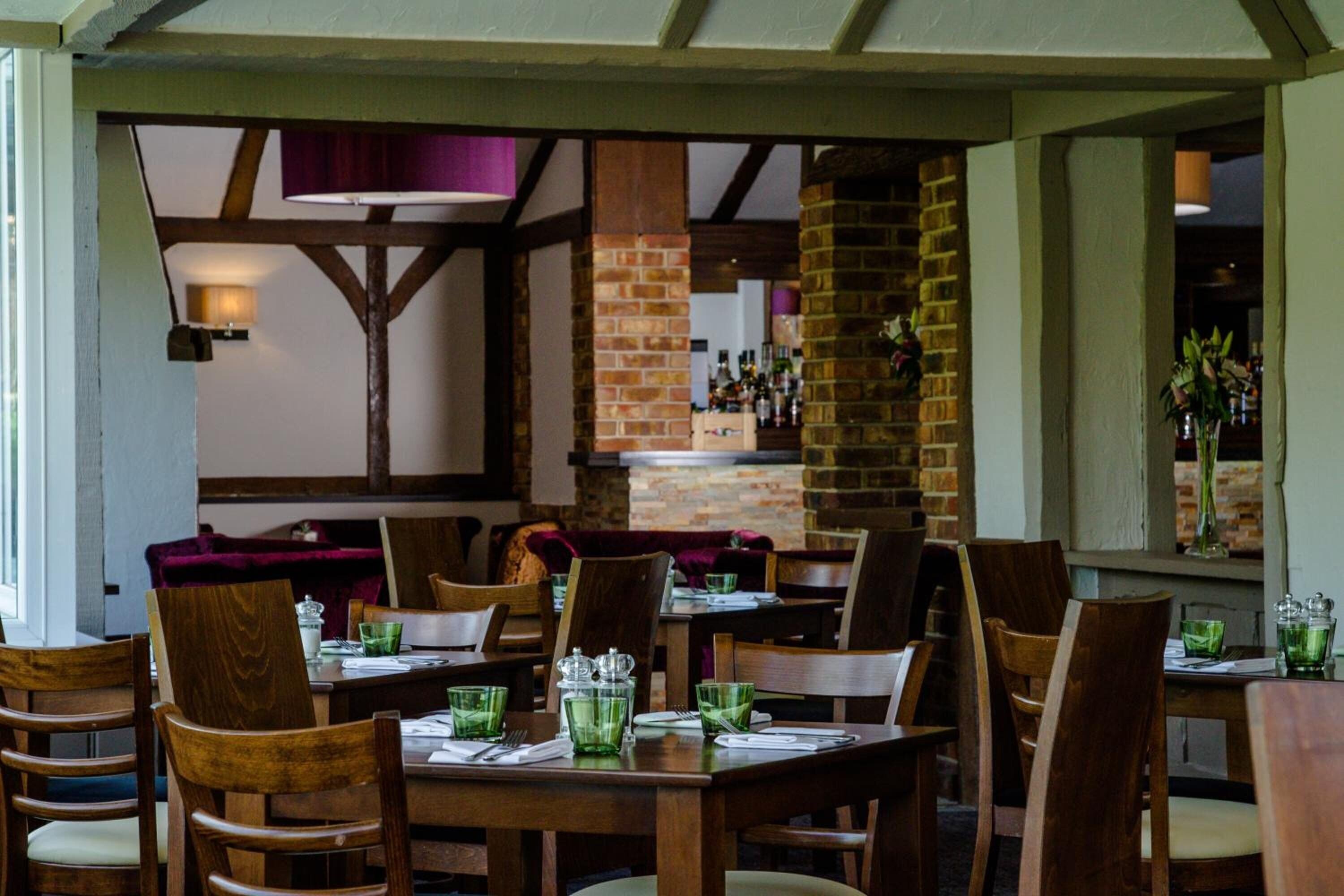 A restaurant interior with wooden tables and chairs, brick walls, and a bar area.