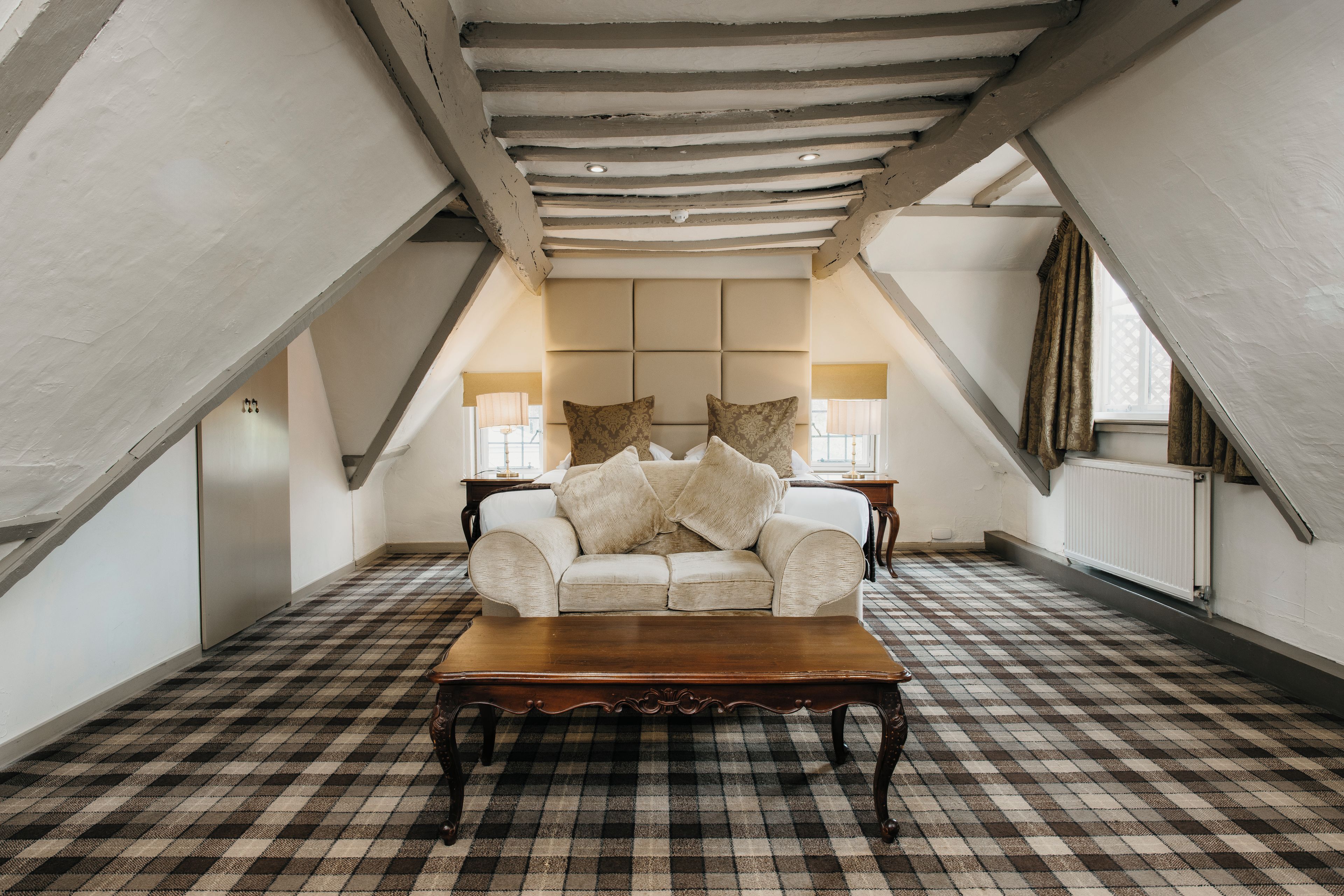 Quarto aconchegante com piso xadrez, um sofá, mesa de centro de madeira e uma cama com cabeceira.