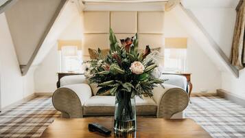 A room with a checkered floor, a wooden coffee table with a vase of flowers, a sofa, and a remote control.
